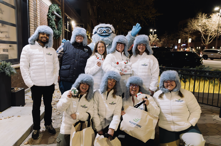 Mascota Yeti con grupo de empleados de Elevations que llevan gorros Ushanka con orejeras y chaquetas con la marca Elevations
