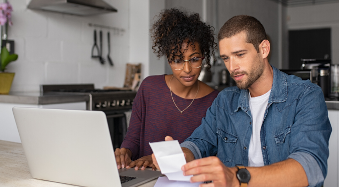 Couple looking at piece of paper with laptop at front. 