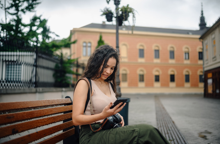 Female looking at phone while resting on a bench in a foreign street. Woman checking her phone while resting in a foreign street