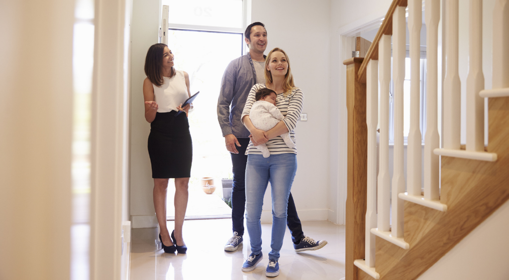 happy couple with baby looking at a home with a realtor