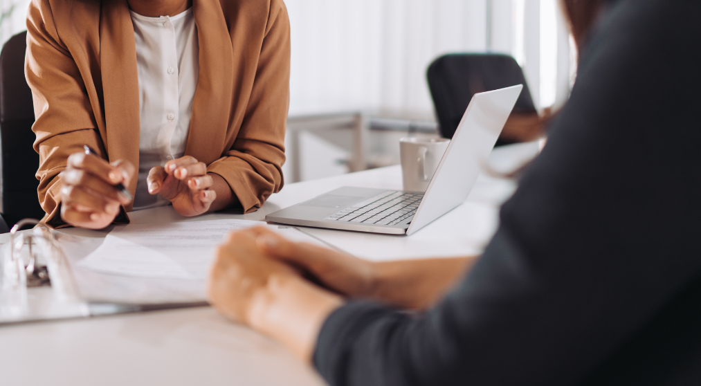 Discussion between two people with papers and laptop on table.