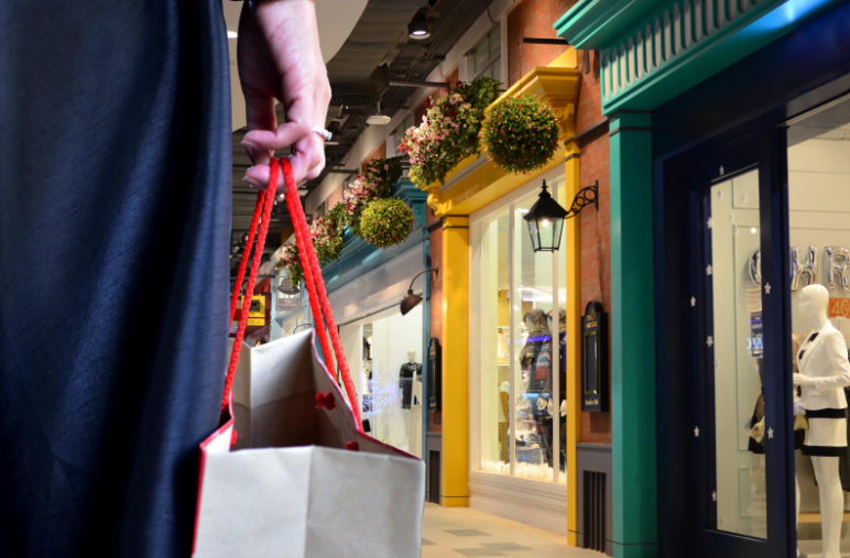A woman carries a bag of shopping down a picturesque row of shops