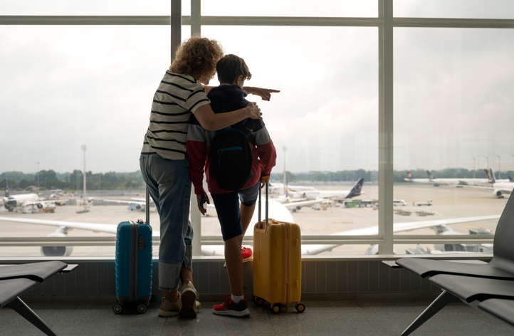 A mother and son watch airplanes prepare for takeoff while waiting in the airport