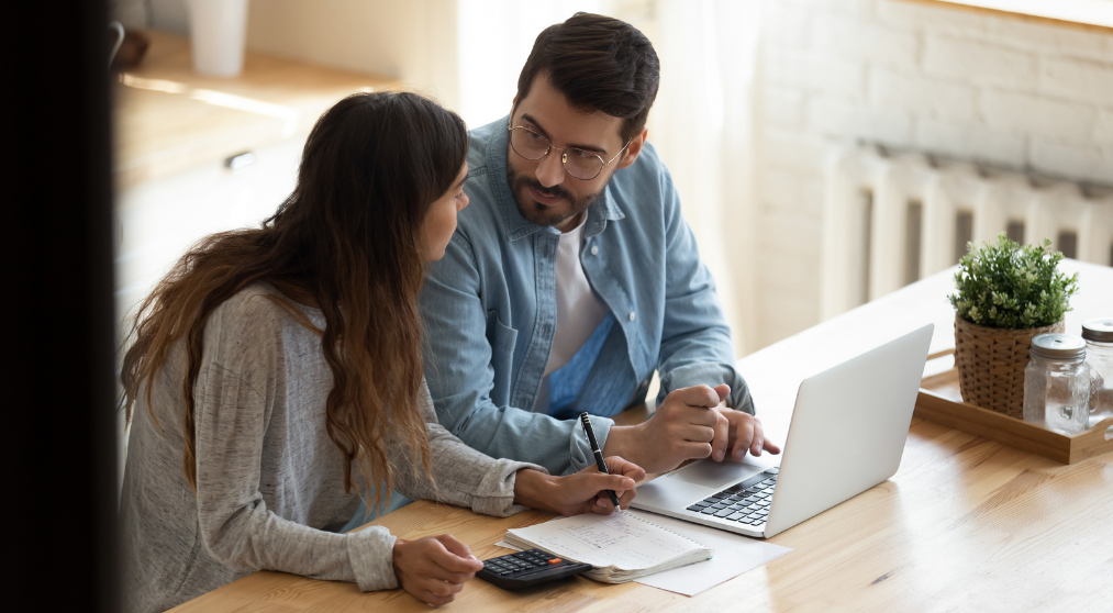 a father and daughter discussing finances at the kitchen table with an open laptop
