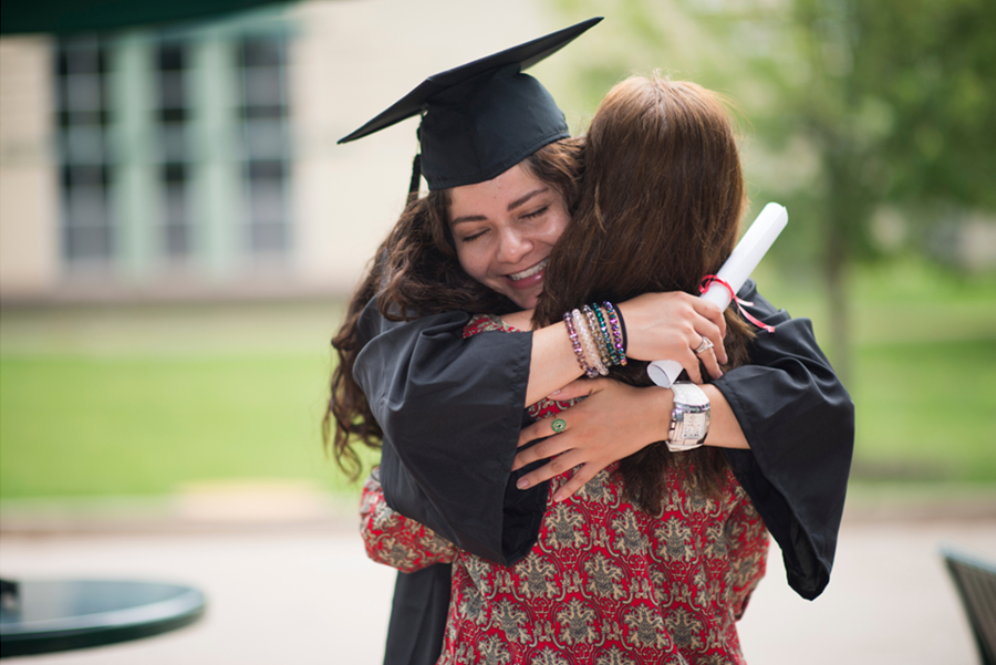 Student in a cap and gown hugging her parent on a spring day