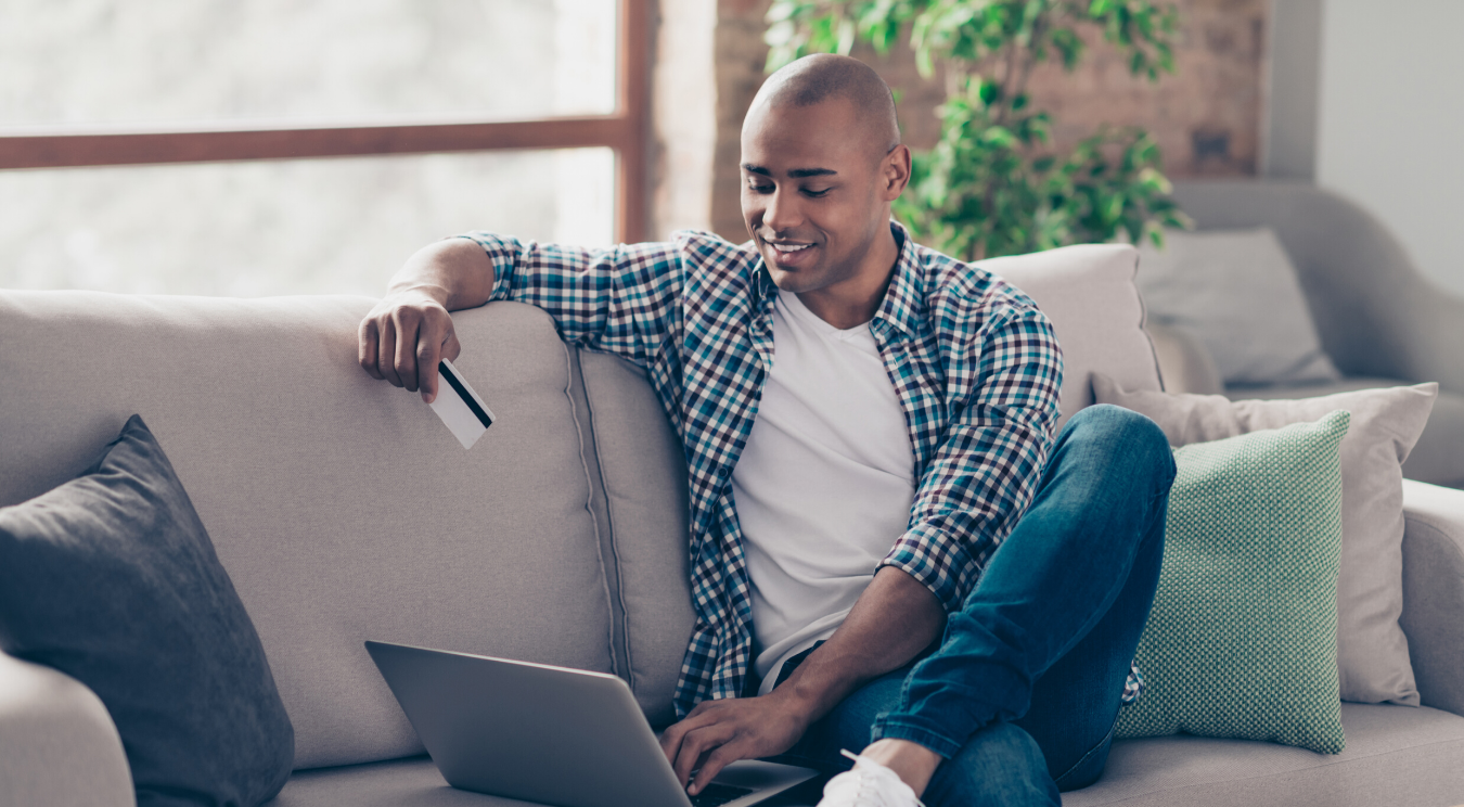 Man sitting on couch with laptop and card.